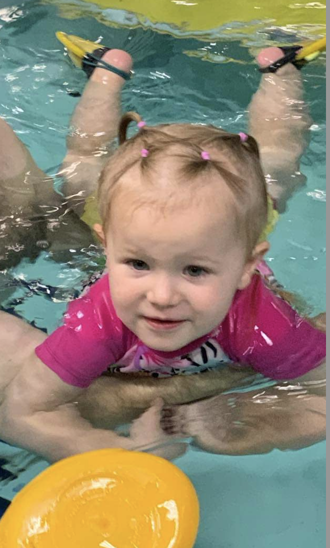 young girl floating in a pool supported by an adult