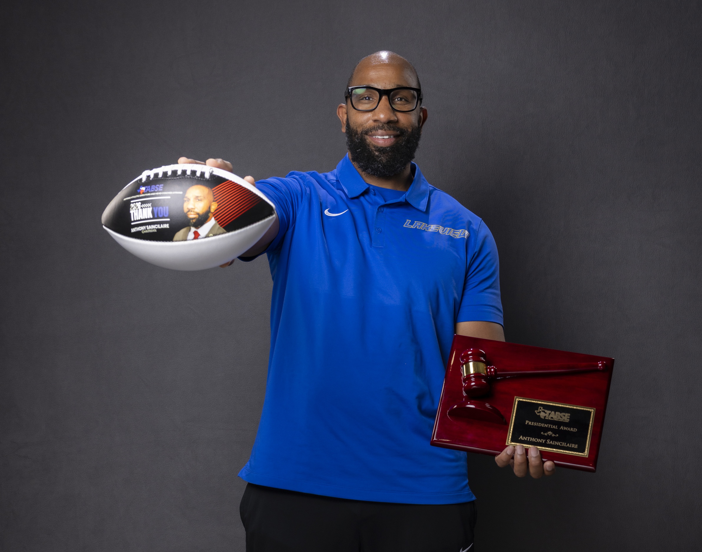 a male adult holds a football and a plaque