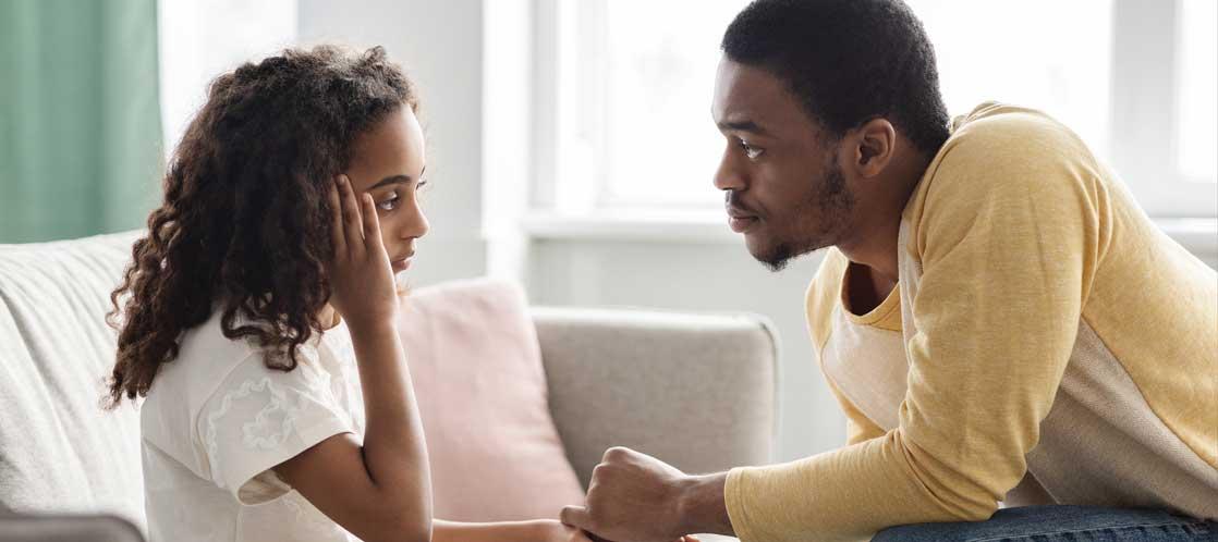 Parent sitting across upset middle school aged girl and holding her hand in curious understanding manner