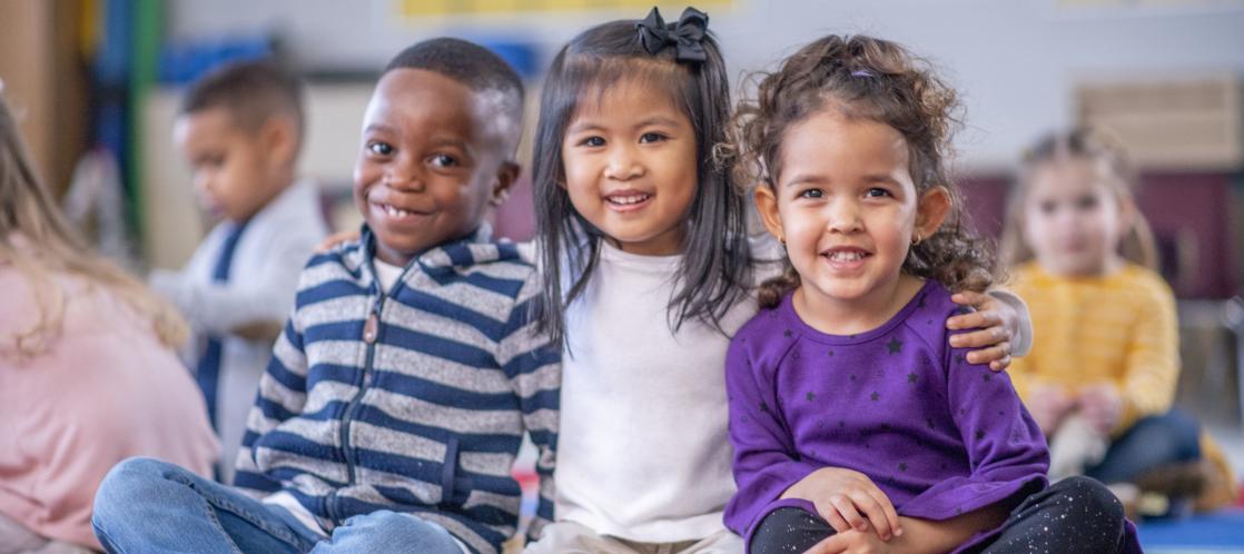 A diverse trio of pre-k students sit posing together