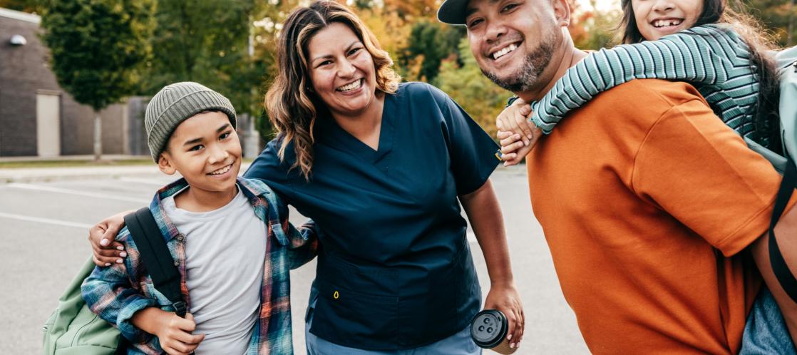 A family of four stands together posing with the father holding the daughter on his back