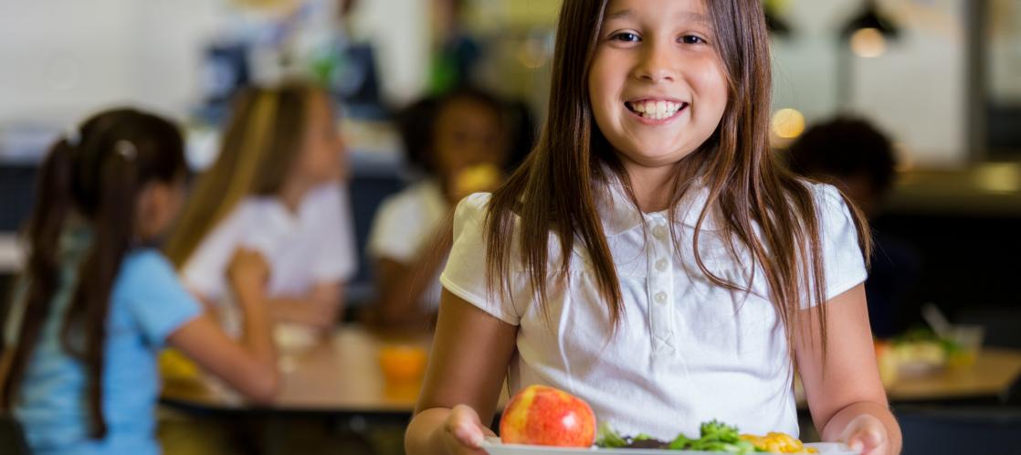 Student holds school lunch tray while smiling