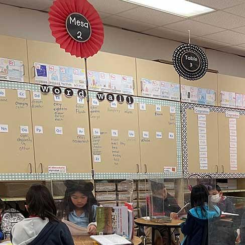 Students sitting at mesa 2 near word wall in dual language classroom at Vial.