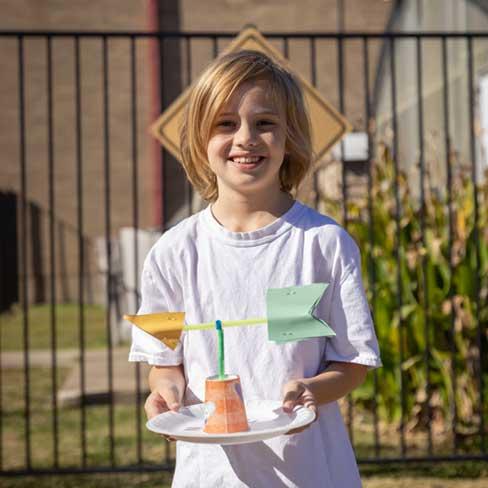 Elementary student displaying paper wind vane project outside of Beaver Math Science and Technology Center.