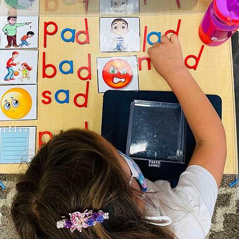 Young girl in Montessori class working with letter manipulatives to spelling words rhyming with pad.