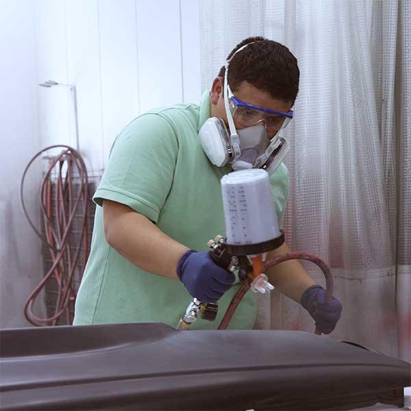 High school boy wearing protective face gear using paint sprayer on the hood of a car.