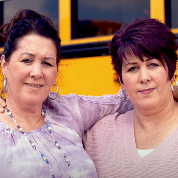 Two staff members sharing a side hug in front of a bus