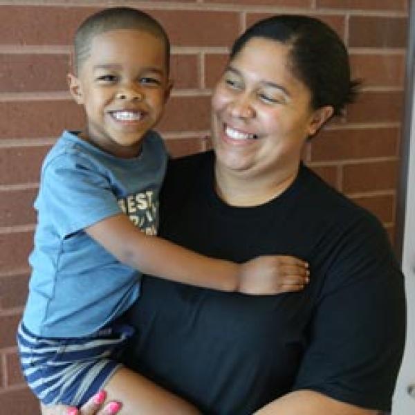 A mom smiling while holding her toddler at a school