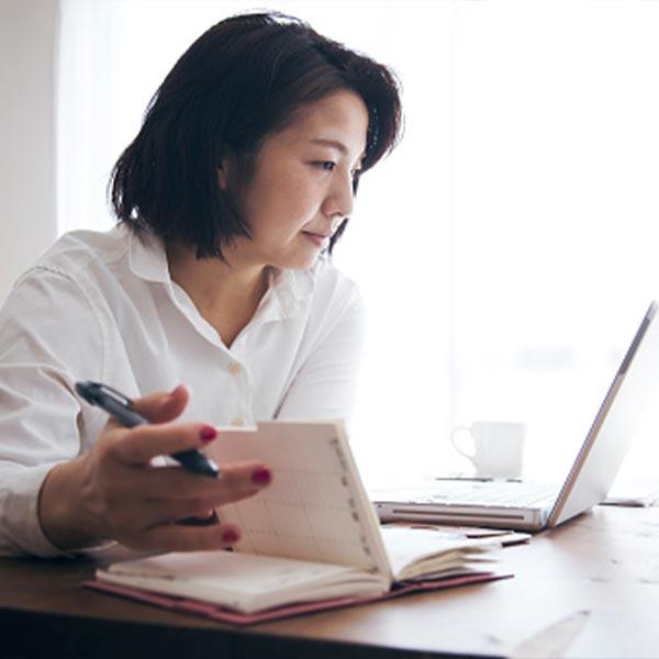 A woman flipping through a notebook while looking at a computer.