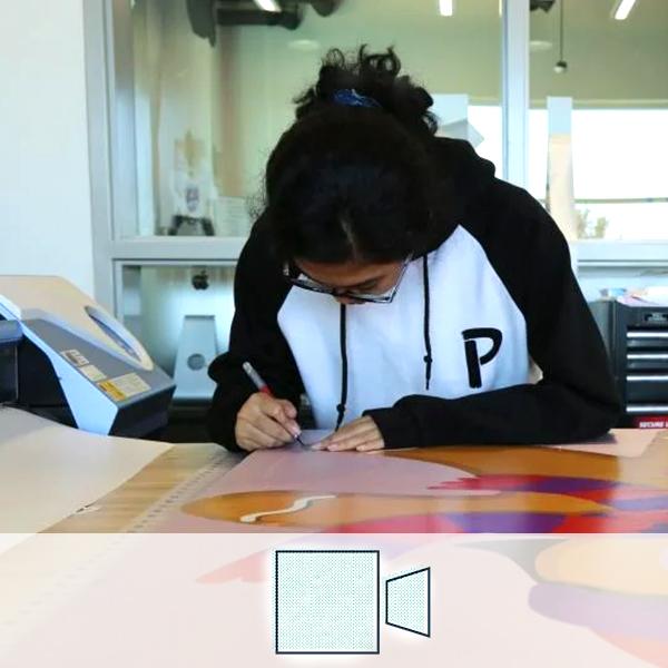 A girl working on cutting out a print in printing/imaging. A camera icon representing the Arts and A/V cluster is overlaid on the image.