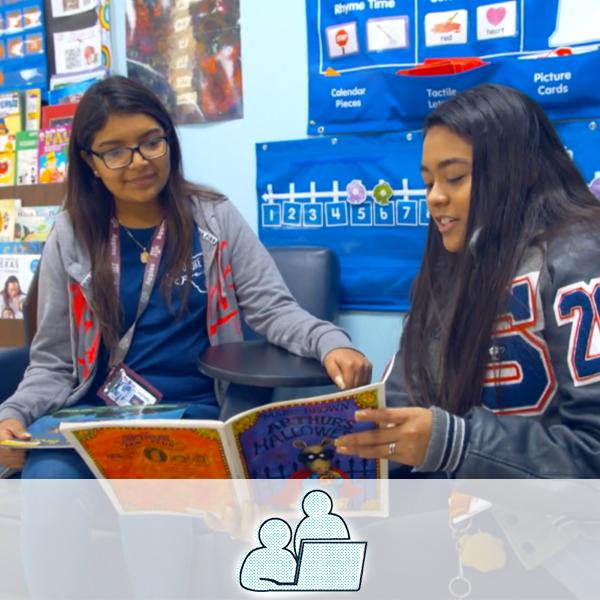 A student practicing giving a lesson to her teacher. An icon of two people with a laptop is overlaid on the image,  representing the education cluster.