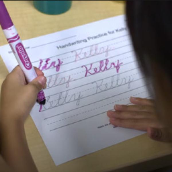 A student practicing writing a name.