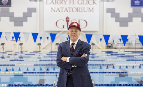 Man stands in front of pool and a large sign that reads Larry H. Glick Natatorium