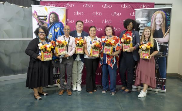 A seven-member diverse group of men and women stand holding gifts