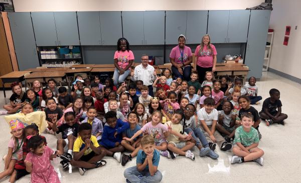 A large group of students sit with four adults kneeling behind them