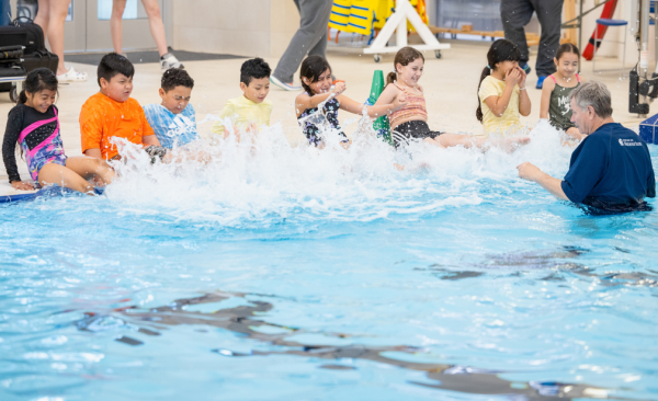 A diverse group of students kick their feet in the water of a pool