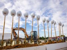 With construction equipment in the background, a row of helmets on shovel handles stand ready for the RHS MAC groundbreaking ceremony.