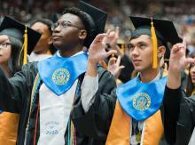 Two young men at graduation ceremony wearing Collegiate Academy collars with their cap and gown.