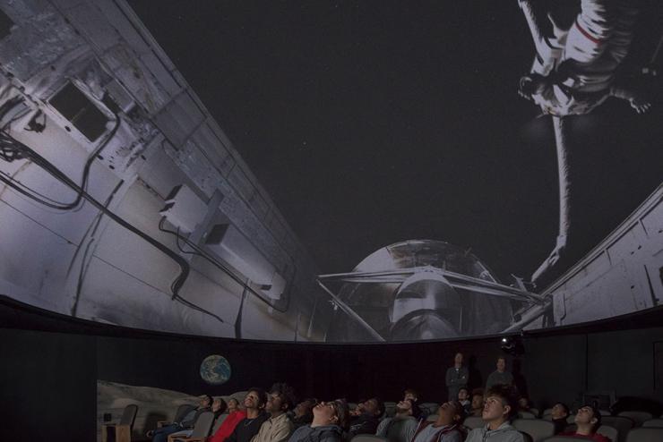 Students look up at dome screen displaying space shuttle and astronaut.