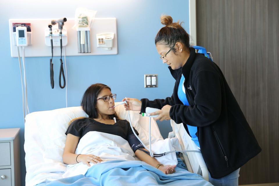 A student taking the blood pressure and temperature of another student in a hospital bed