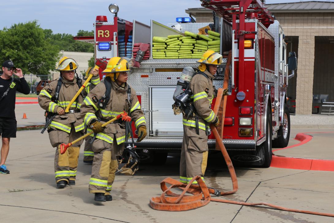 Students in firefighter gear taking a hose from a firetruck