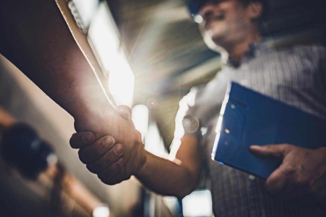 Close up of hand shake with man holding a notebook