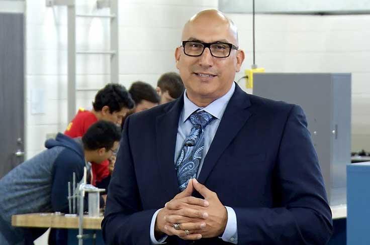 Dr. Lopez smiling at the camera with GRCTC students working in the background