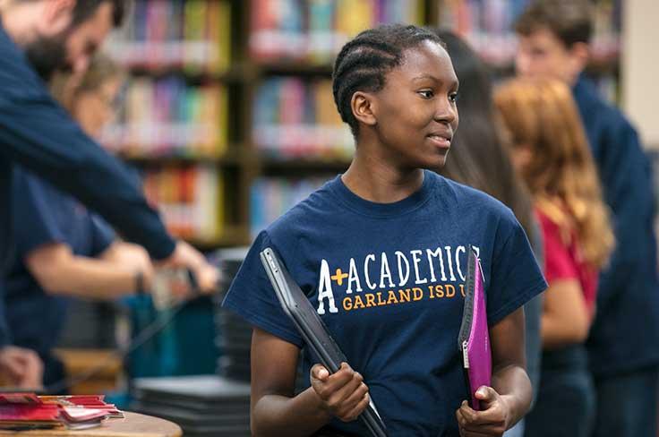 High school girl in library wearing A+ Academics Garland ISD t-shirt