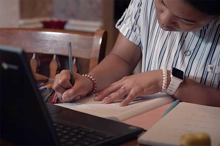 Close up of a girl writing on a paper near laptop