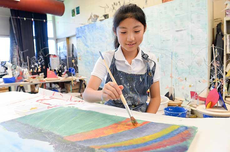 Girl painting in art class in middle school classical program.