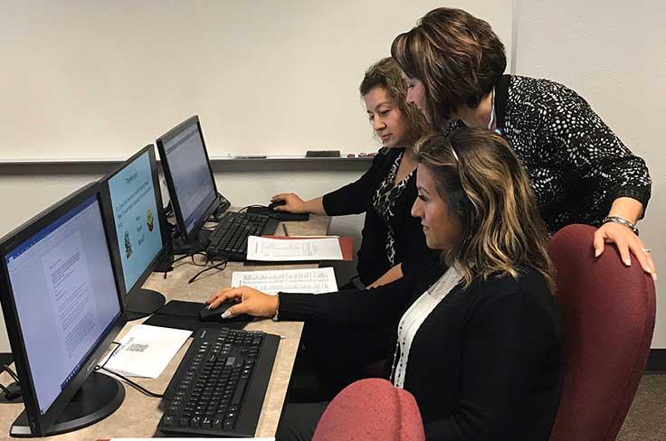 Staff training session with presenter leaning over to assist two employees at computers