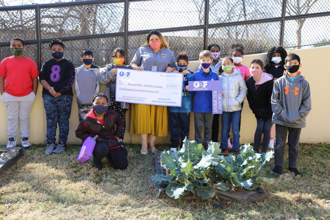 Teacher and students hold GEF grant check by school garden