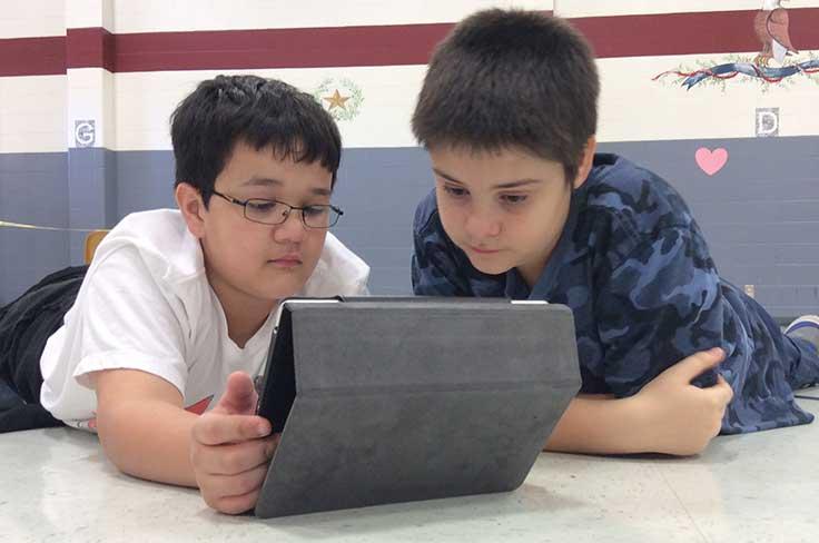 Two elementary boys staring intently at an iPad.