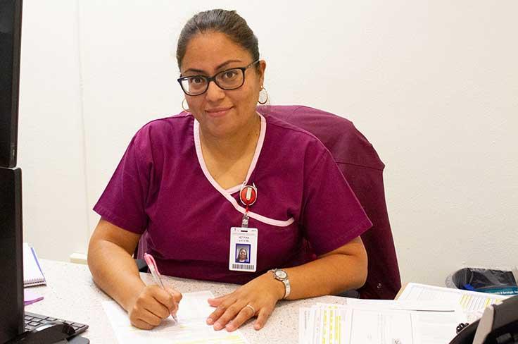 Seated nurse from enrollment center clinic smiling at camera.