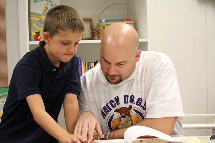 A volunteer dad wearing a Watch D.O.G.S shirt working with an elementary boy student