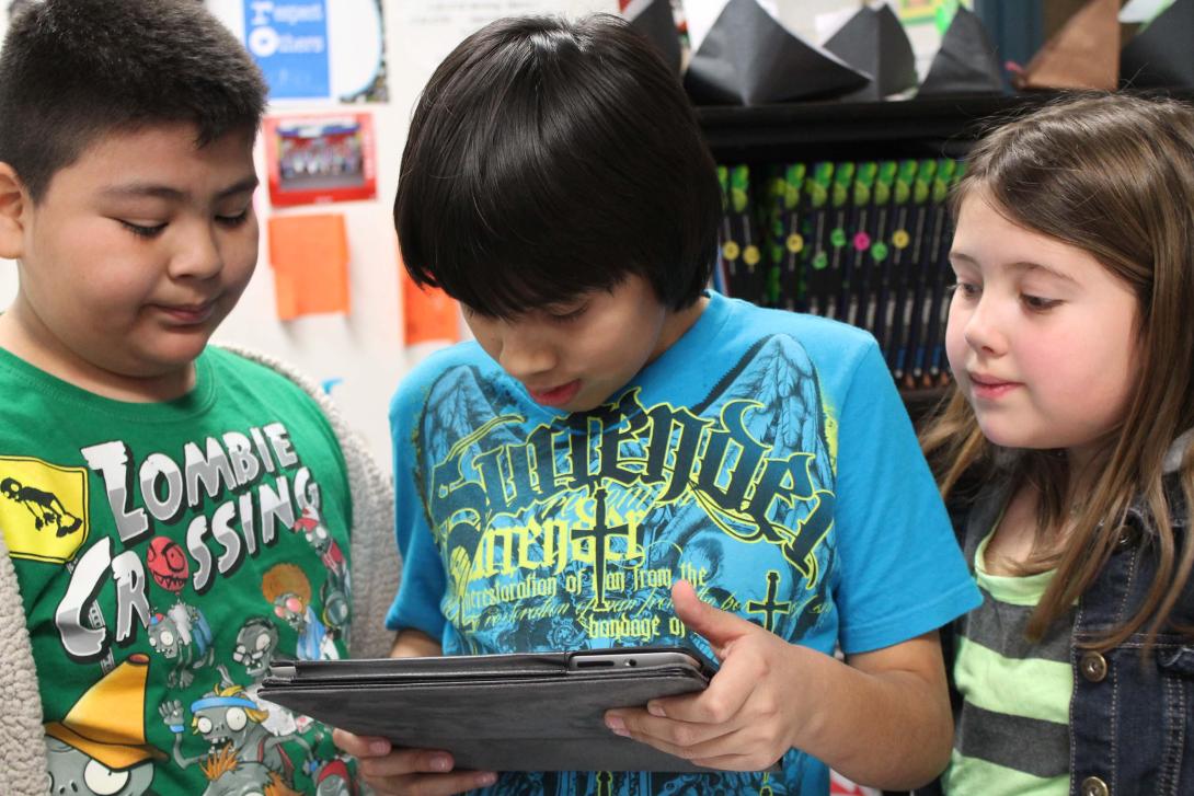 Three smiling kids using an iPad