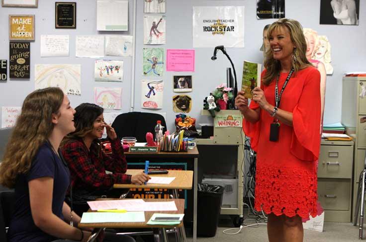 High school English teacher smiling as she holds up book for students.