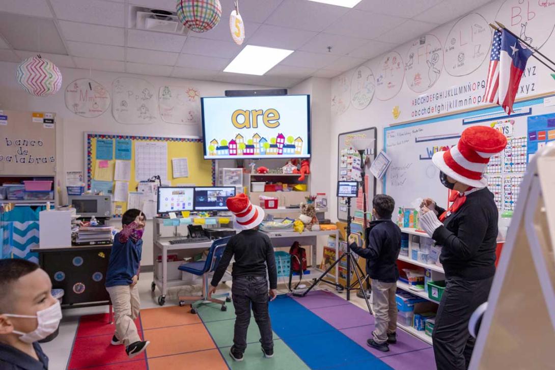 Elementary students standing for interactive lesson displayed on large classroom screen.