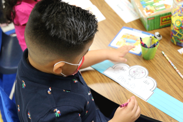 A student coloring in a paper crown that says "Pre-K"