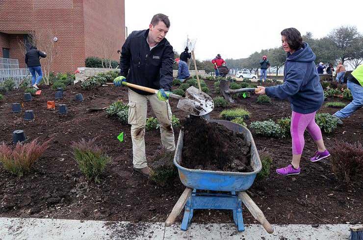 Man and woman shoveling dirt into wheelbarrow while helping with school garden