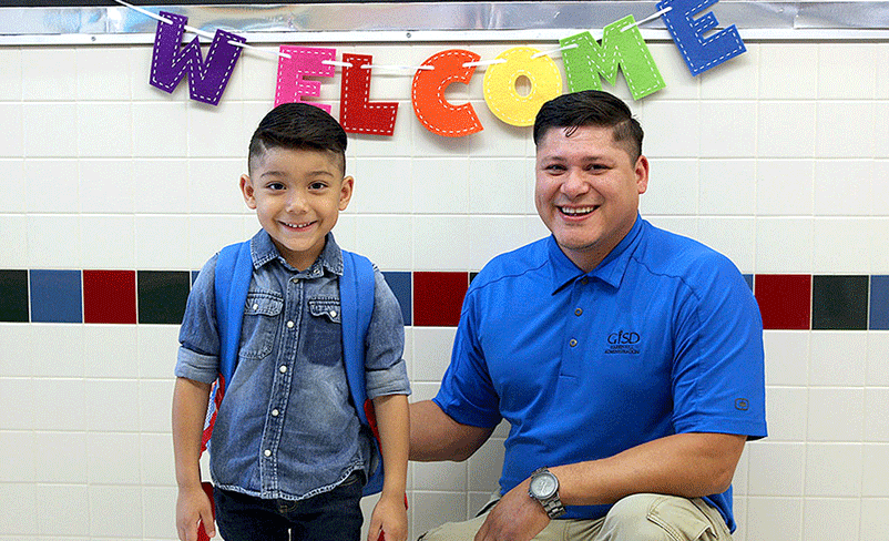 A dad and his son posing in front of a welcome sign on the first day of school