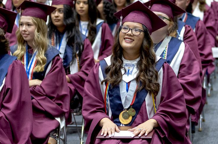 A student smiling with other graduates a seated crowd