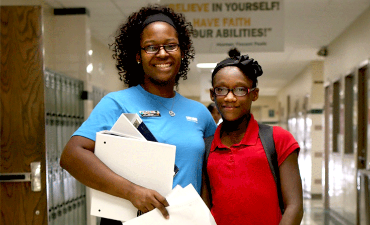 A mom smiling with her daughter in the hallway with school supplies