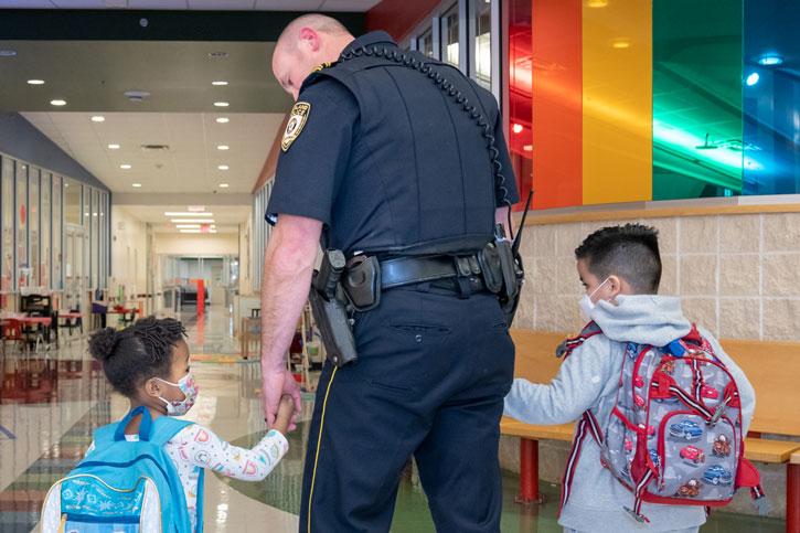 A Security Resource Officer holding the hands of Pre-K kids while walking down the hall