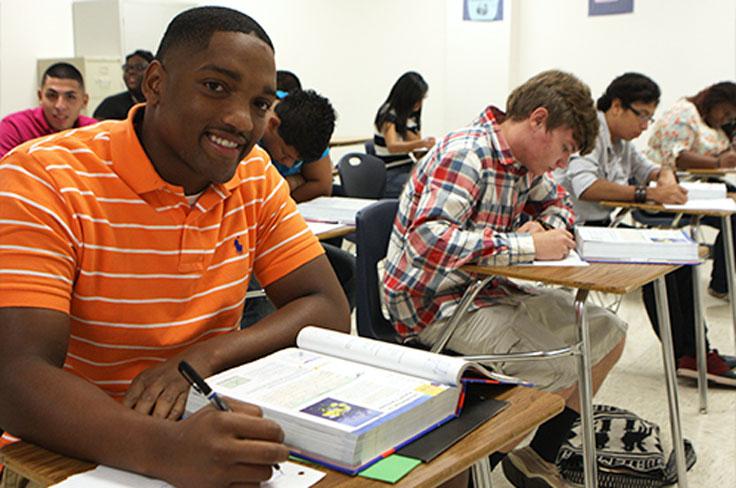 A student smiling while taking notes out of a textbook in class