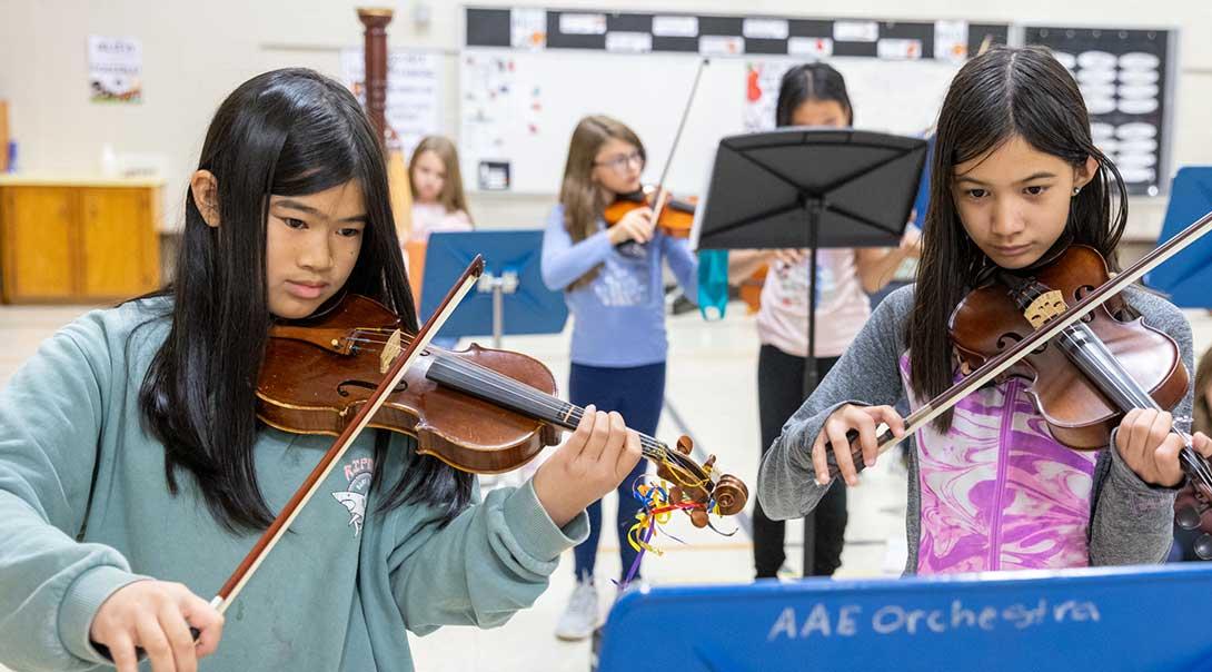 Two middle school students playing violin sheet music.