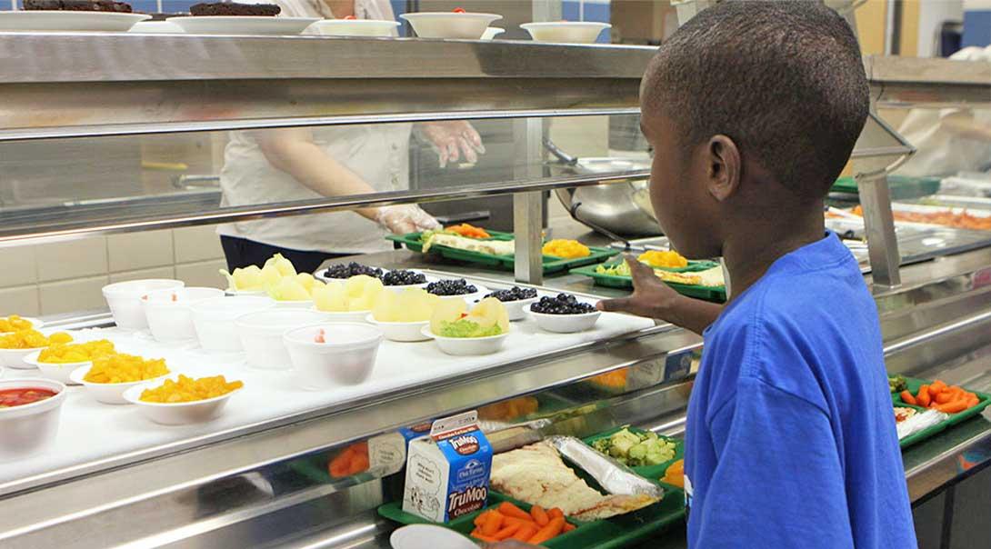 An elementary student reaching for blueberries in the lunch line.