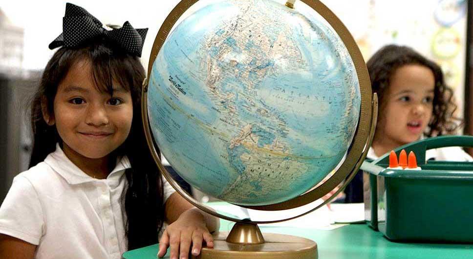 A smiling girl at her desk posing next to a globe