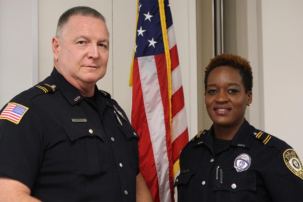 A Caucasian male and African American female Security Resource Officer in front of a flag.