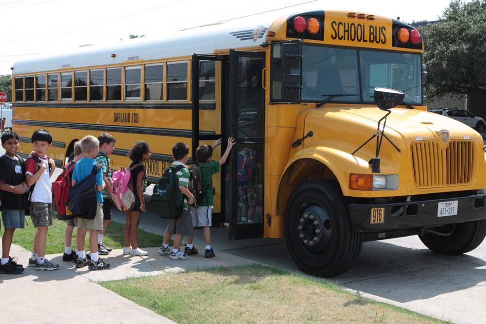 Young students with backpacks lined up to board a bus.